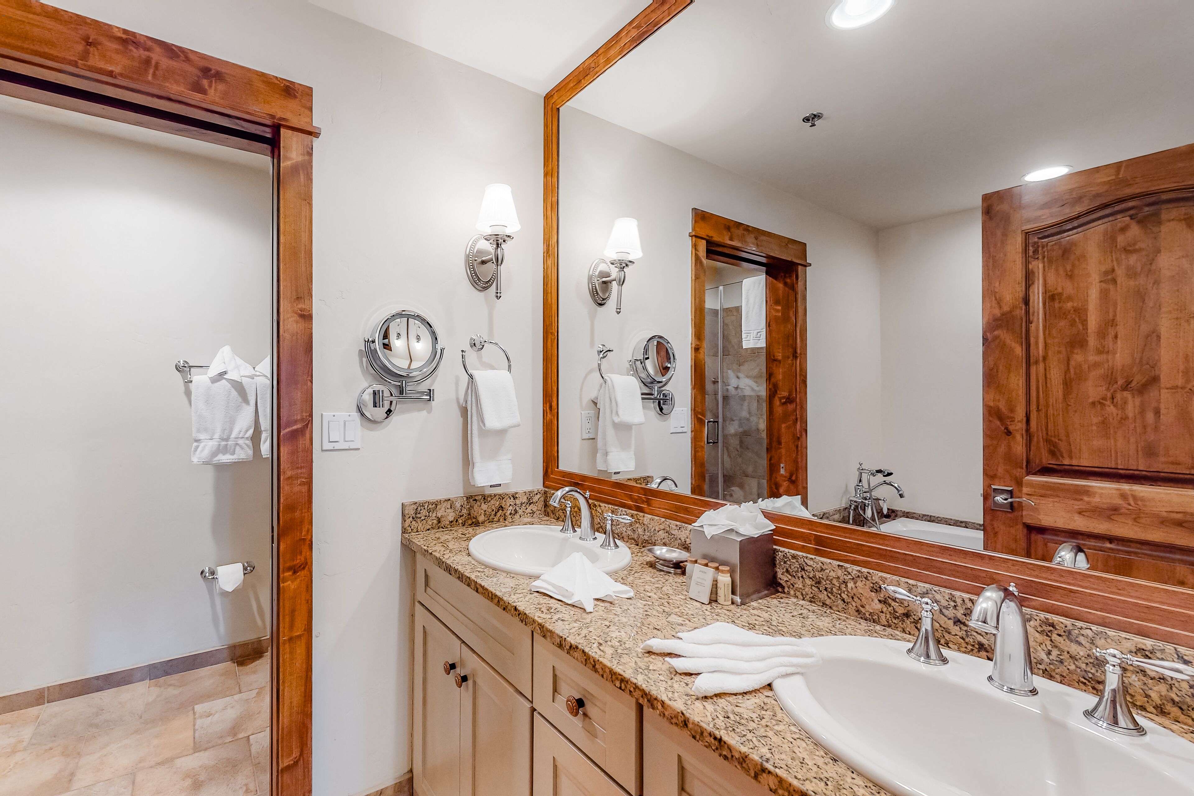 A bathroom with a double sink, two wall-mounted lights, a large mirror, and wooden doors.