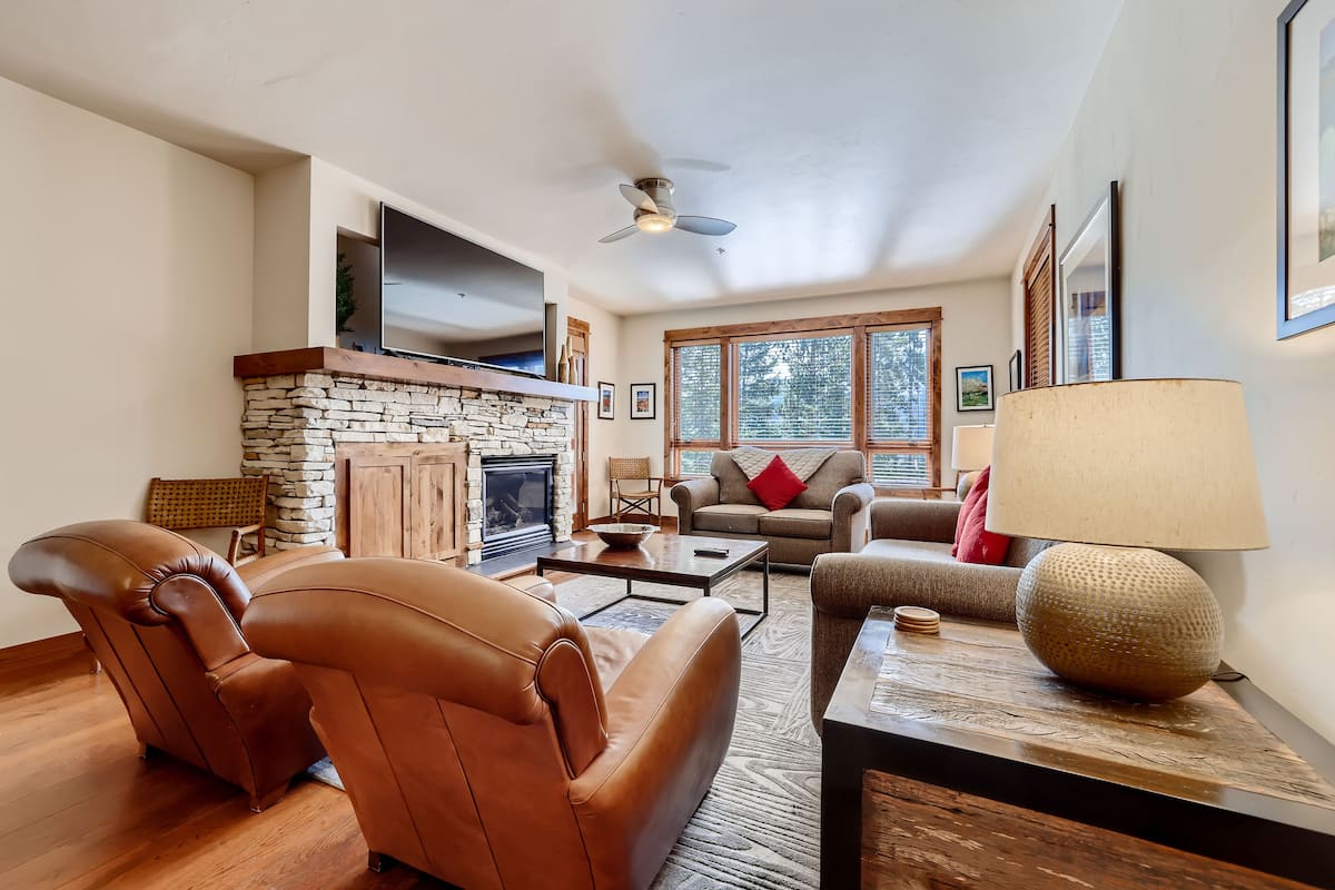 A living room with a stone fireplace, leather chairs, a sofa, a coffee table, and a lamp.
