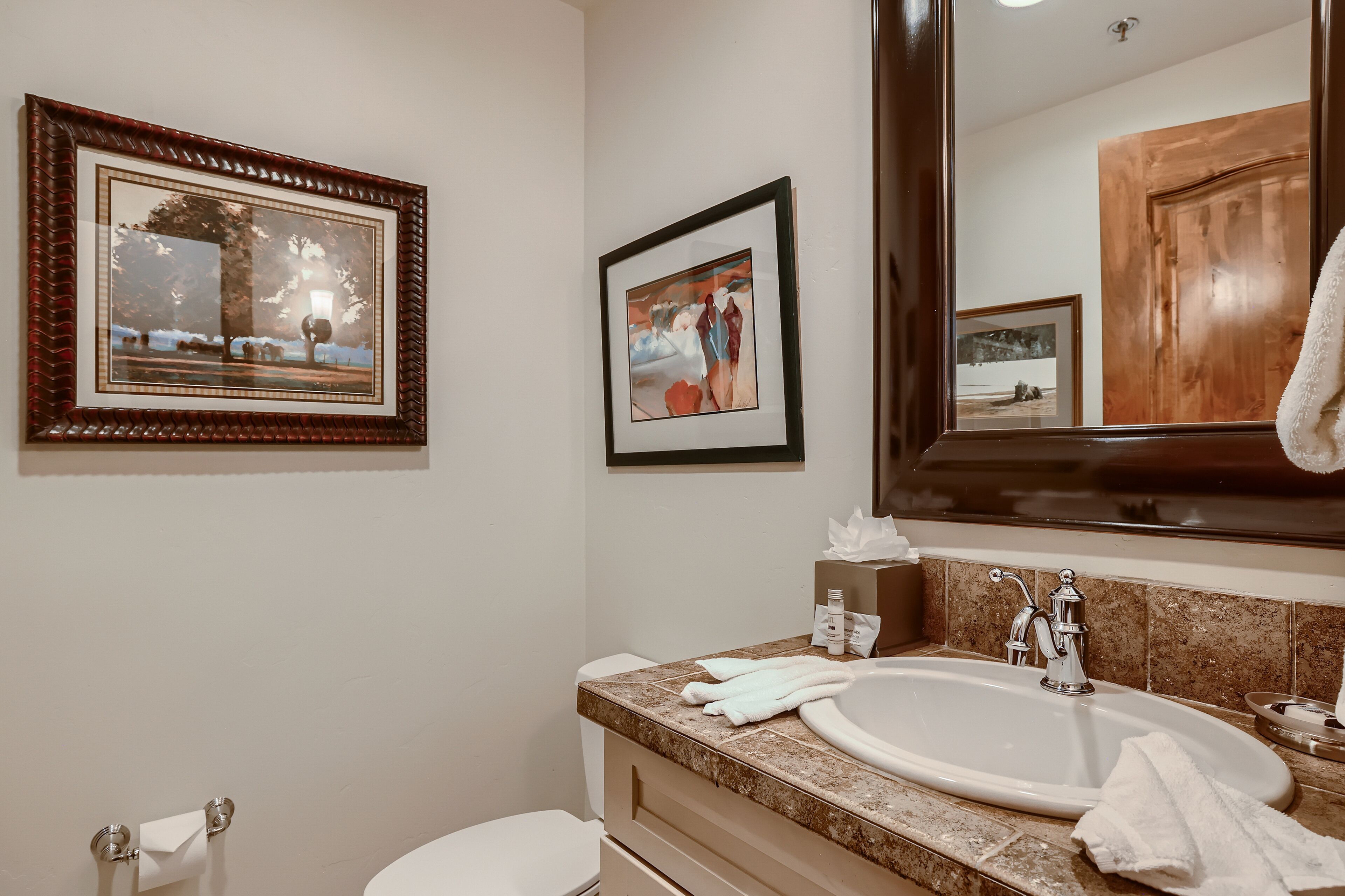 A bathroom with a sink, mirror, and two framed pictures on the wall.