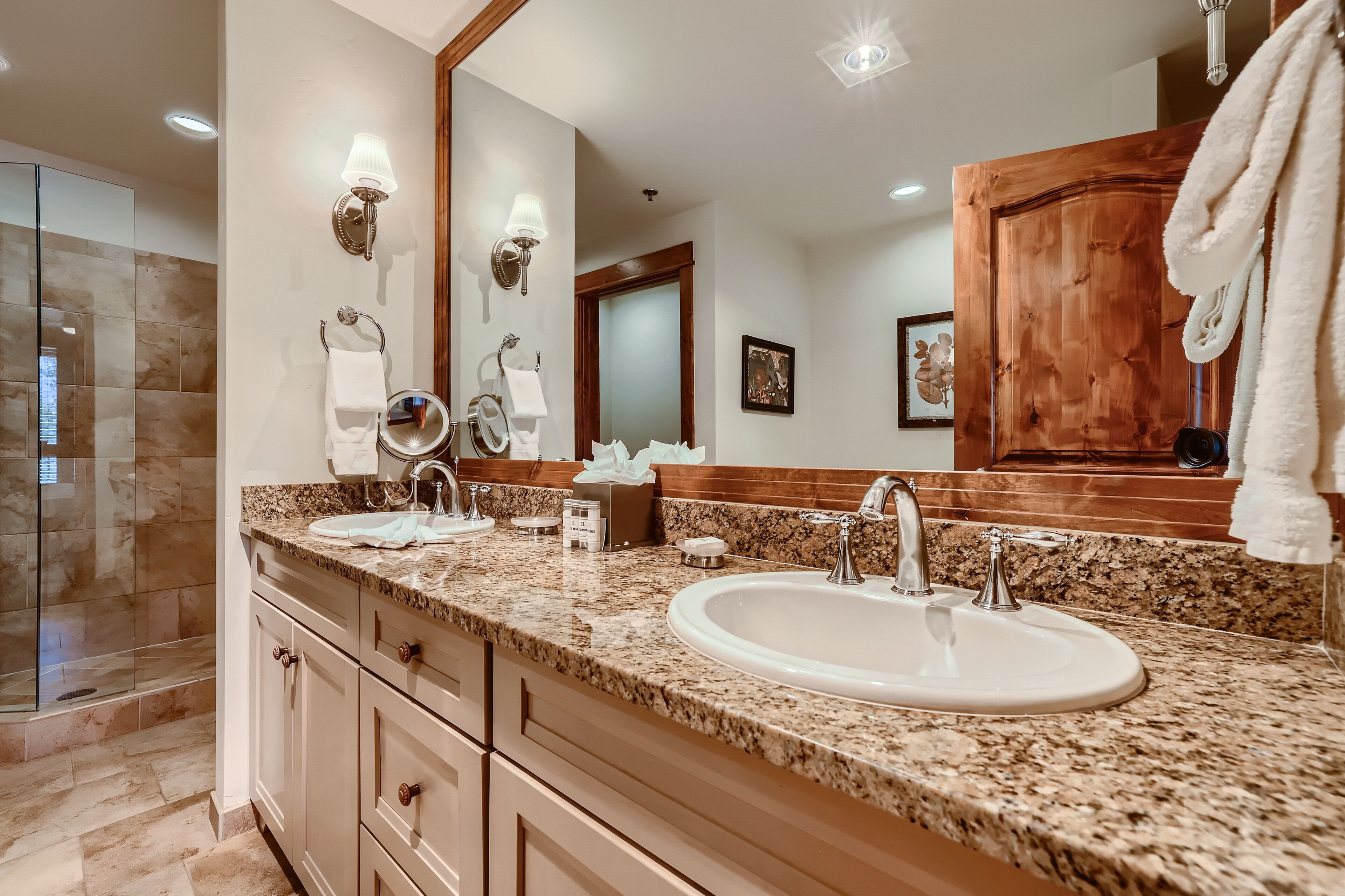 Un baño con encimera de granito, lavabo, espejo y puerta de madera.
