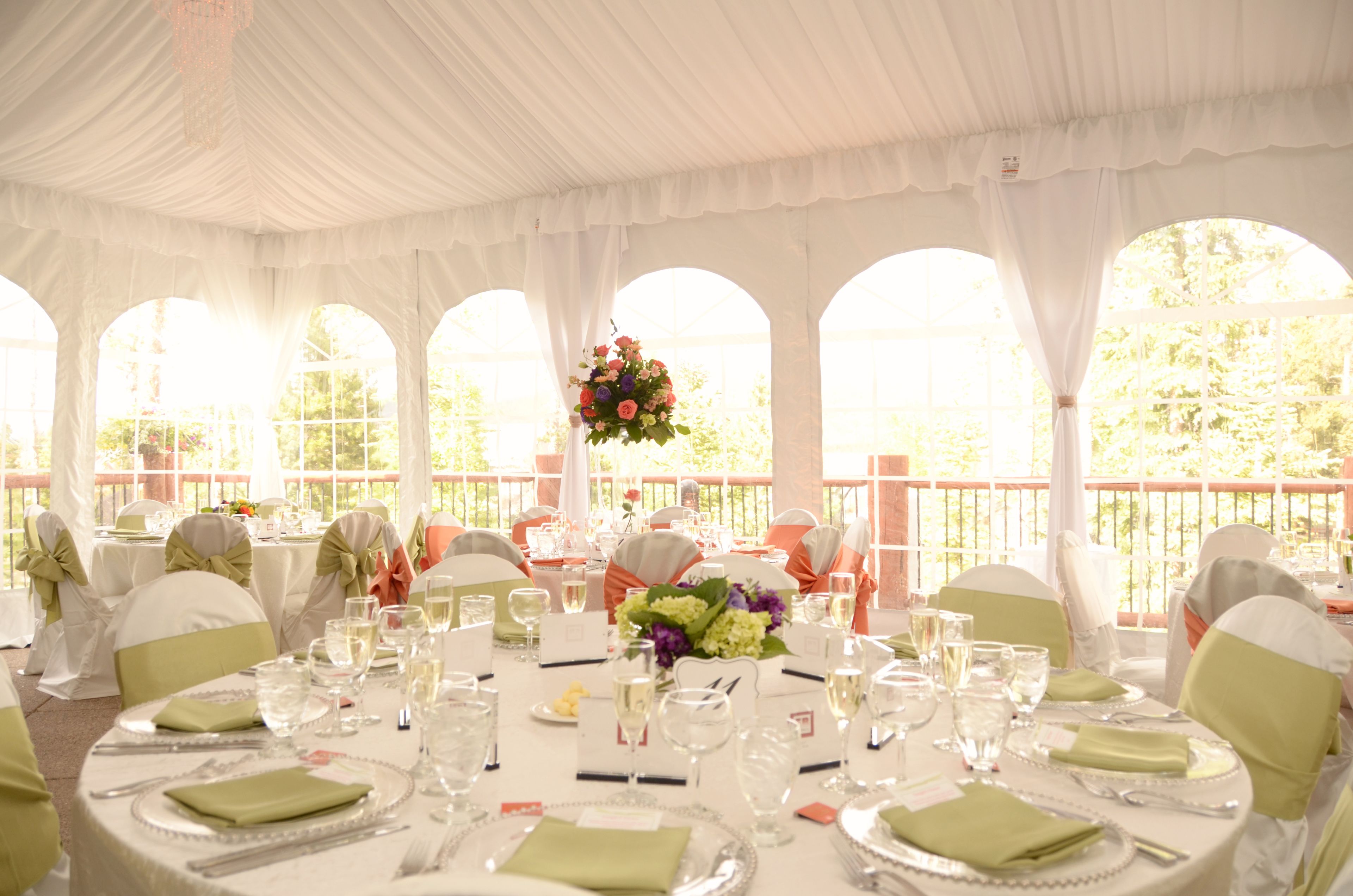 A banquet hall with round tables set for a formal event, featuring white tablecloths, green napkins, and floral centerpieces.