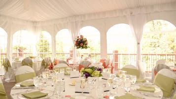 A banquet hall with round tables set for a formal event, featuring white tablecloths, green napkins, and floral centerpieces.