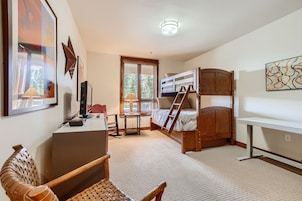 A compact bedroom with bunk beds, a desk, a chair, and a window with blinds.