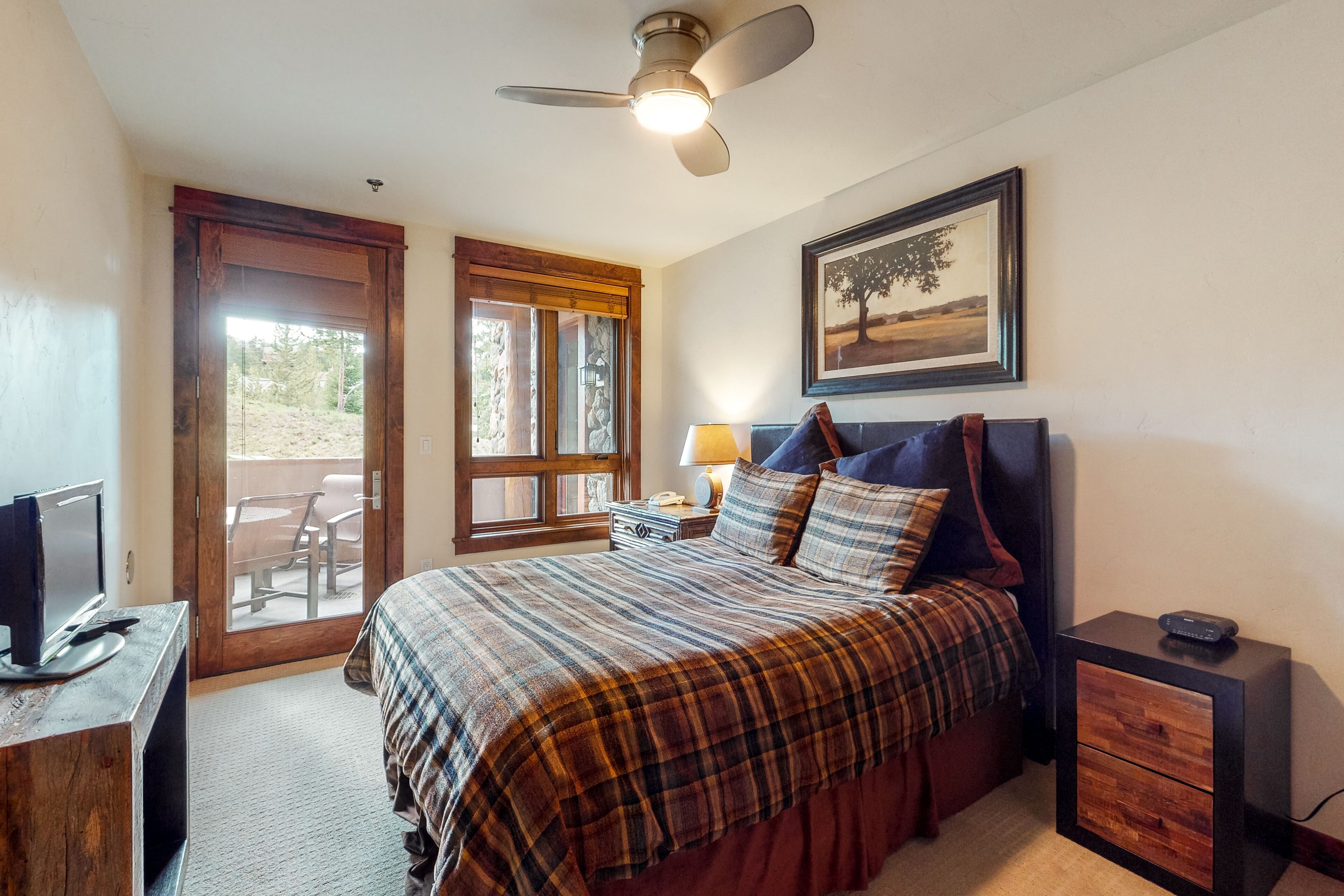 A bedroom with a bed, a desk with a computer, a nightstand, a lamp, and a ceiling fan.