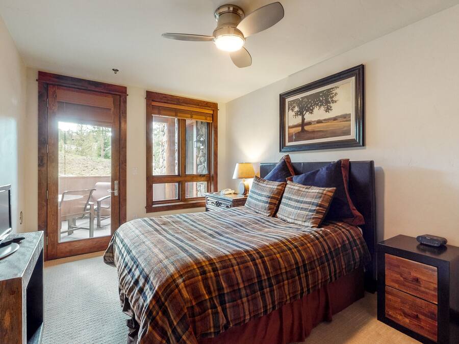 A bedroom with a bed, a desk with a computer, a nightstand, a lamp, and a ceiling fan.