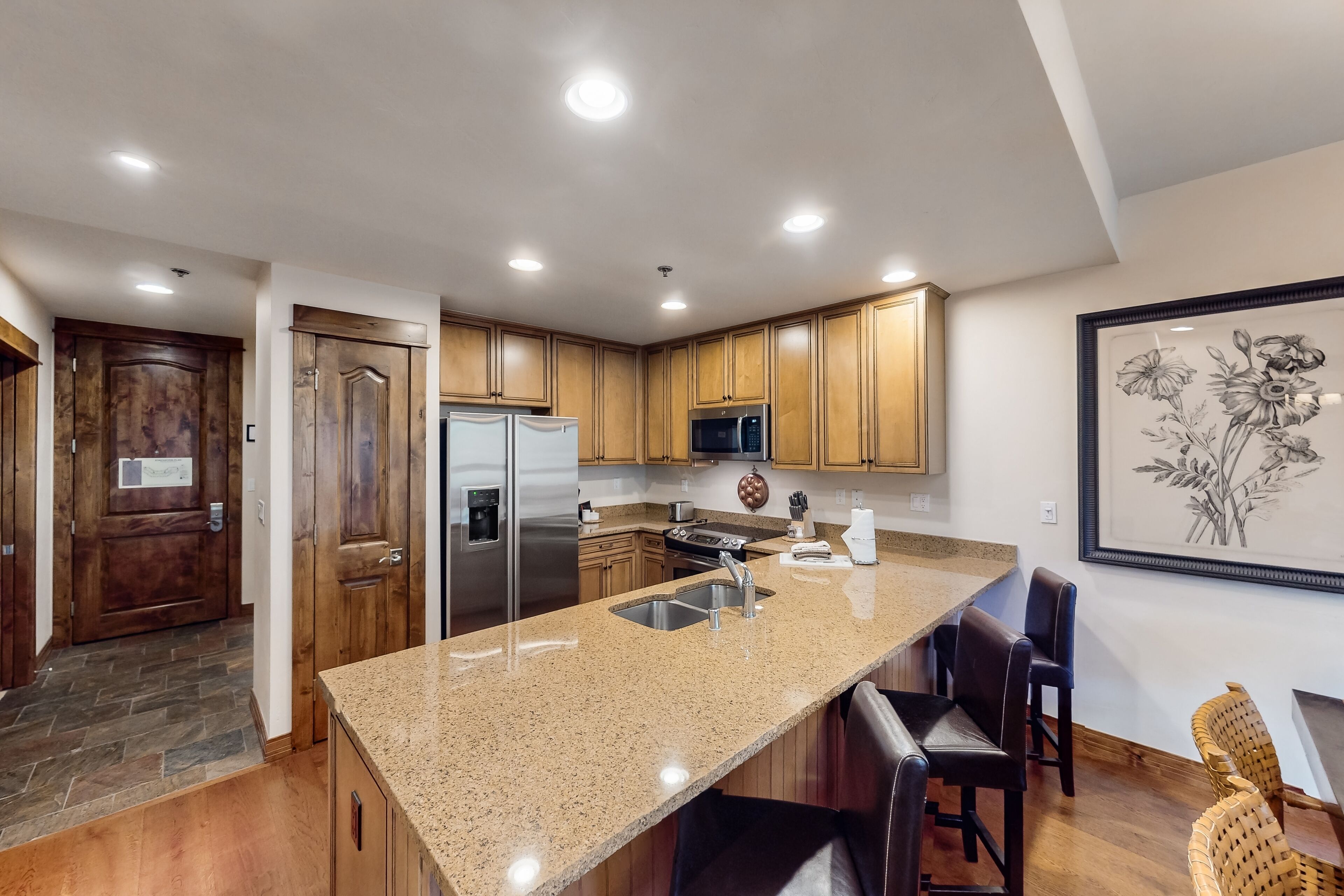 A modern kitchen with granite countertops, stainless steel appliances, wooden cabinets, and a large island with bar seating.