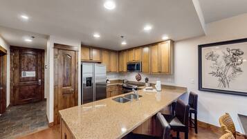 A modern kitchen with granite countertops, stainless steel appliances, wooden cabinets, and a large island with bar seating.