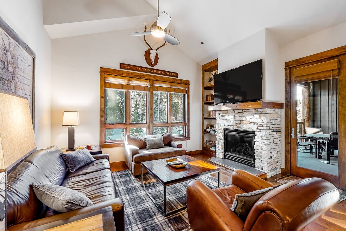 A spacious living room with a fireplace, leather sofas, a coffee table, and a mounted television.