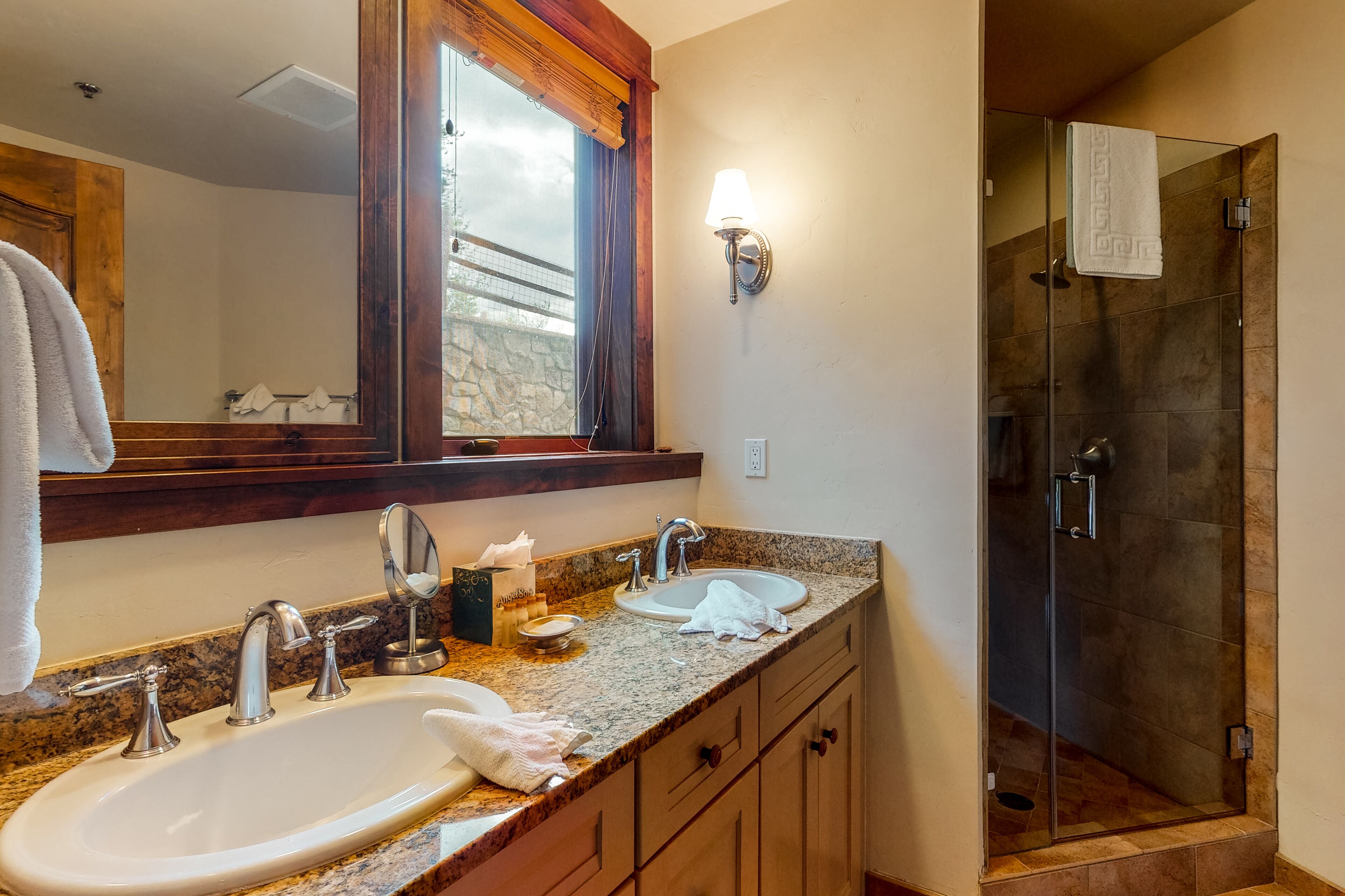 A bathroom with a large mirror, two sinks, a shower, and a towel rack.
