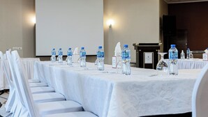 Uma sala de conferências com uma mesa comprida, garrafas de água e uma tela de projeção.