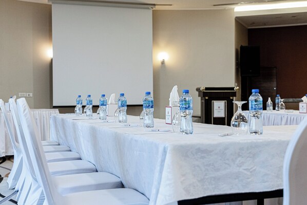 Un salón de conferencias con una larga mesa, botellas de agua y una pantalla de proyector.