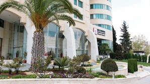 Um hotel moderno com um pátio central que apresenta palmeiras, uma fonte e diversas plantas.