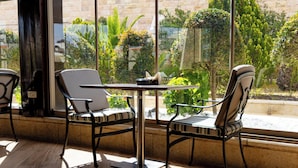 Um quarto com uma mesa e duas cadeiras, uma janela com vista para o verde, e uma parede de pedra.