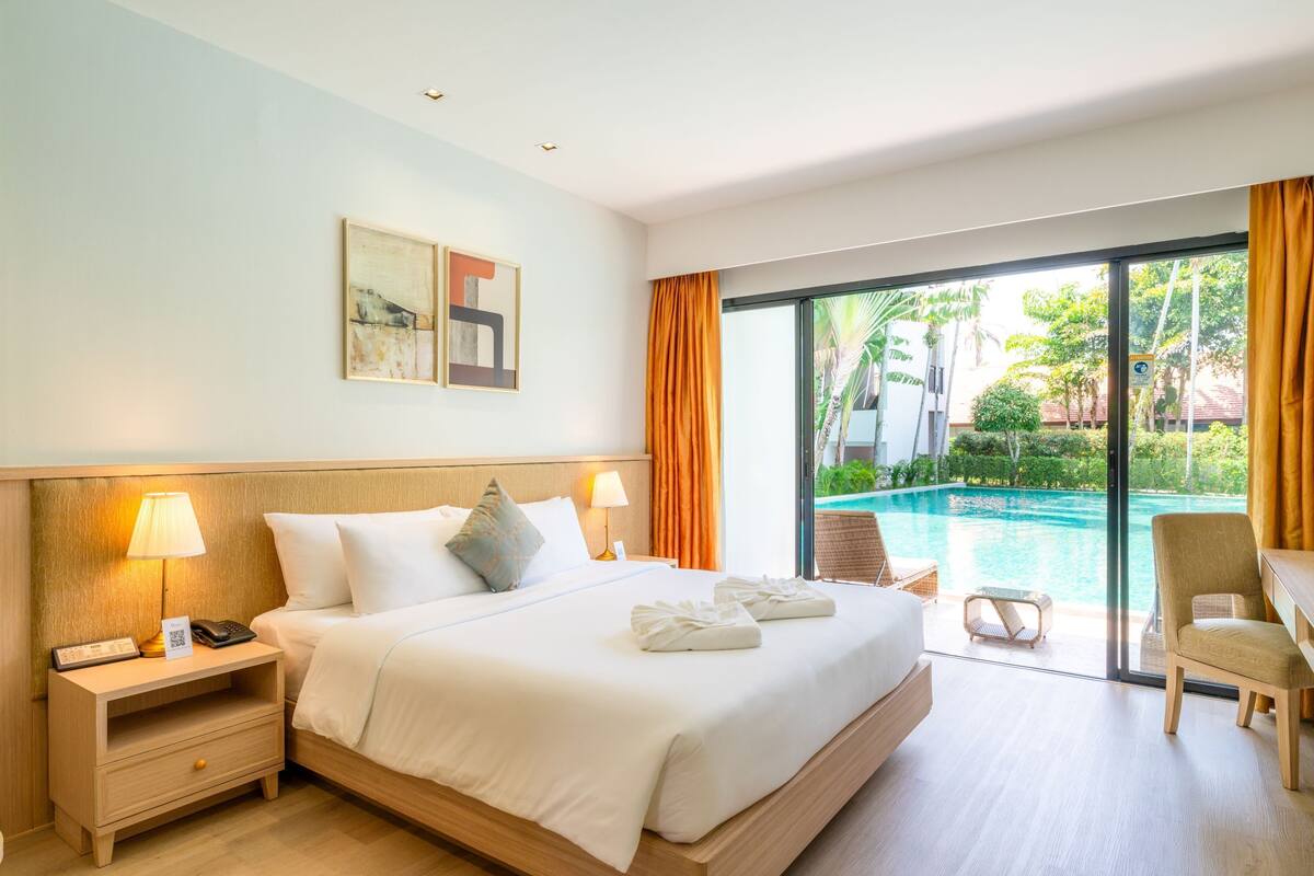 Habitación de hotel con cama, lámparas de noche, escritorio, silla, vista a la piscina y puerta corredera.