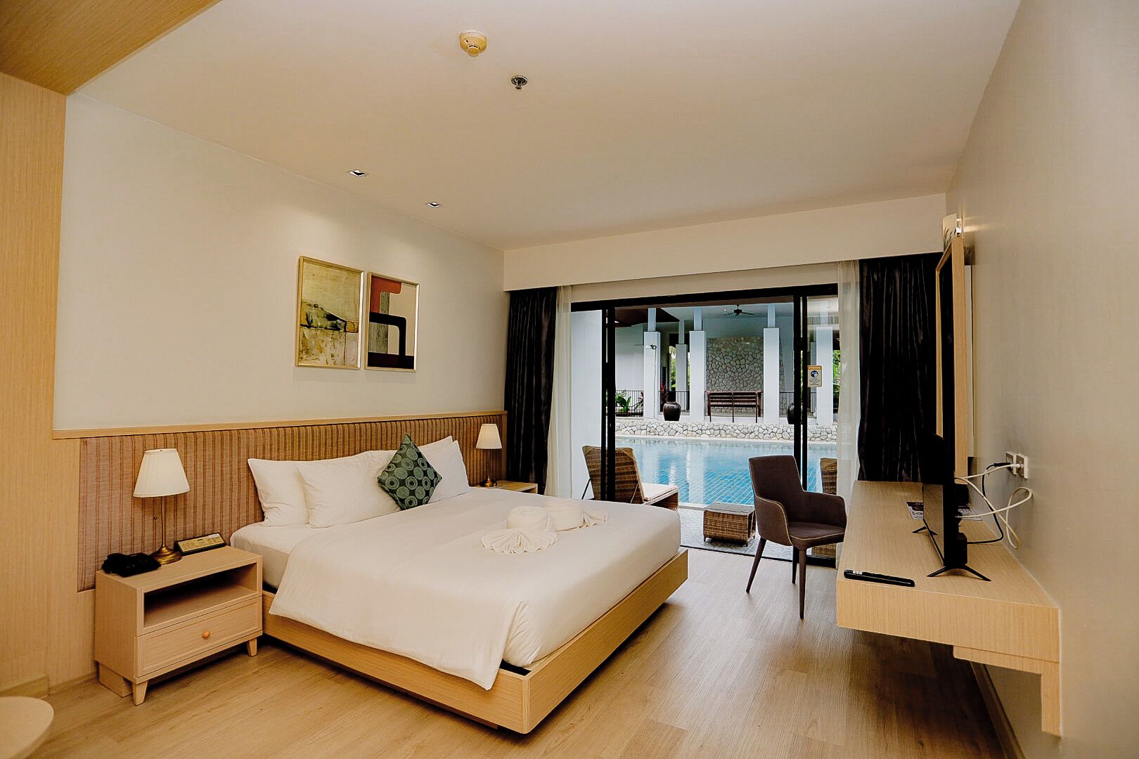 Habitación de hotel con cama, mesitas de noche, un escritorio, una silla y vistas a la zona de piscina.