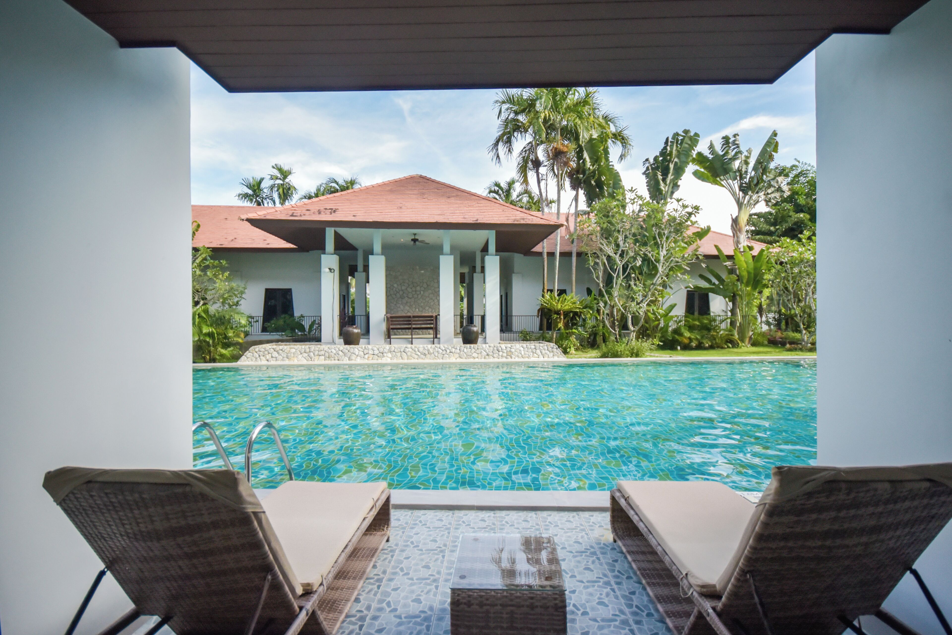 A poolside view with lounge chairs, a clear pool, and a building with a red roof in the background.