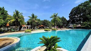A large swimming pool surrounded by palm trees and lounge chairs, with a clear blue sky above. - Estella Phuket Mai Khao Beach Resort (Mai Khao)