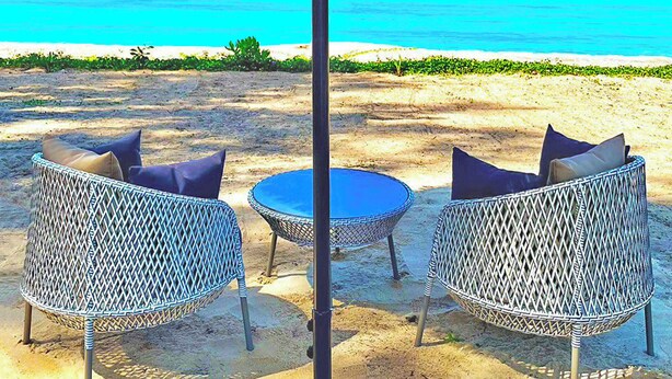 A beachside seating area with a thatched umbrella, two wicker chairs, and a small round table. - Estella Phuket Mai Khao Beach Resort (Mai Khao)