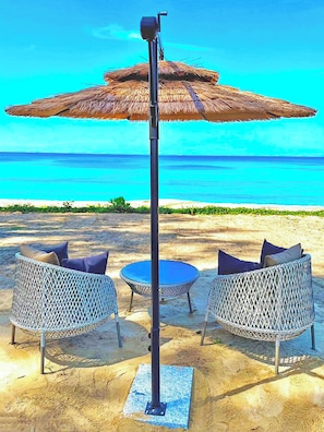 A beachside seating area with a thatched umbrella, two wicker chairs, and a small round table. - Estella Phuket Mai Khao Beach Resort (Mai Khao)
