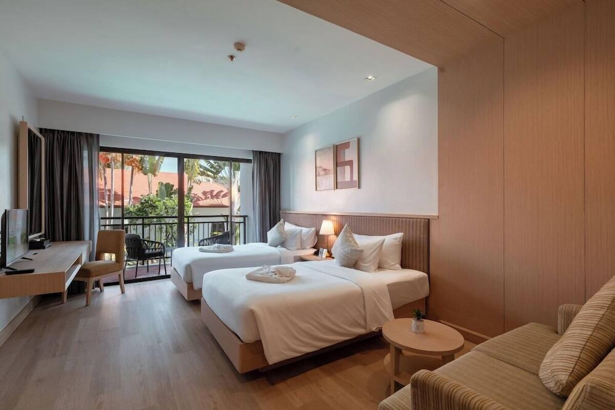 Habitación de hotel con dos camas, un escritorio, una silla, una mesita redonda y un balcón con vistas.