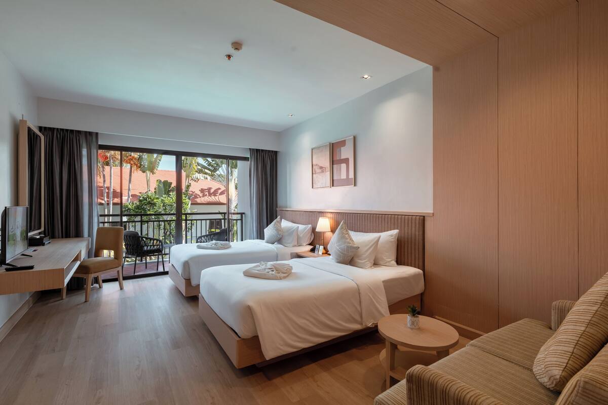 Habitación de hotel con dos camas, un escritorio, una silla, una mesa redonda y un balcón con vistas.