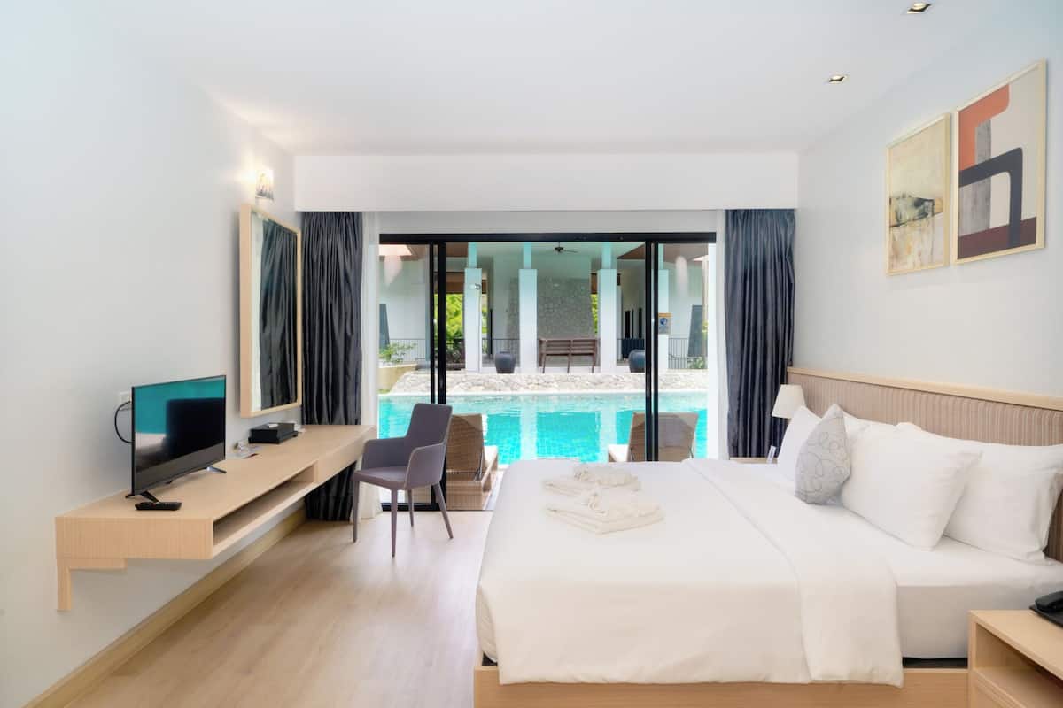 Habitación de hotel con cama, televisión, escritorio, silla y vista a una piscina.