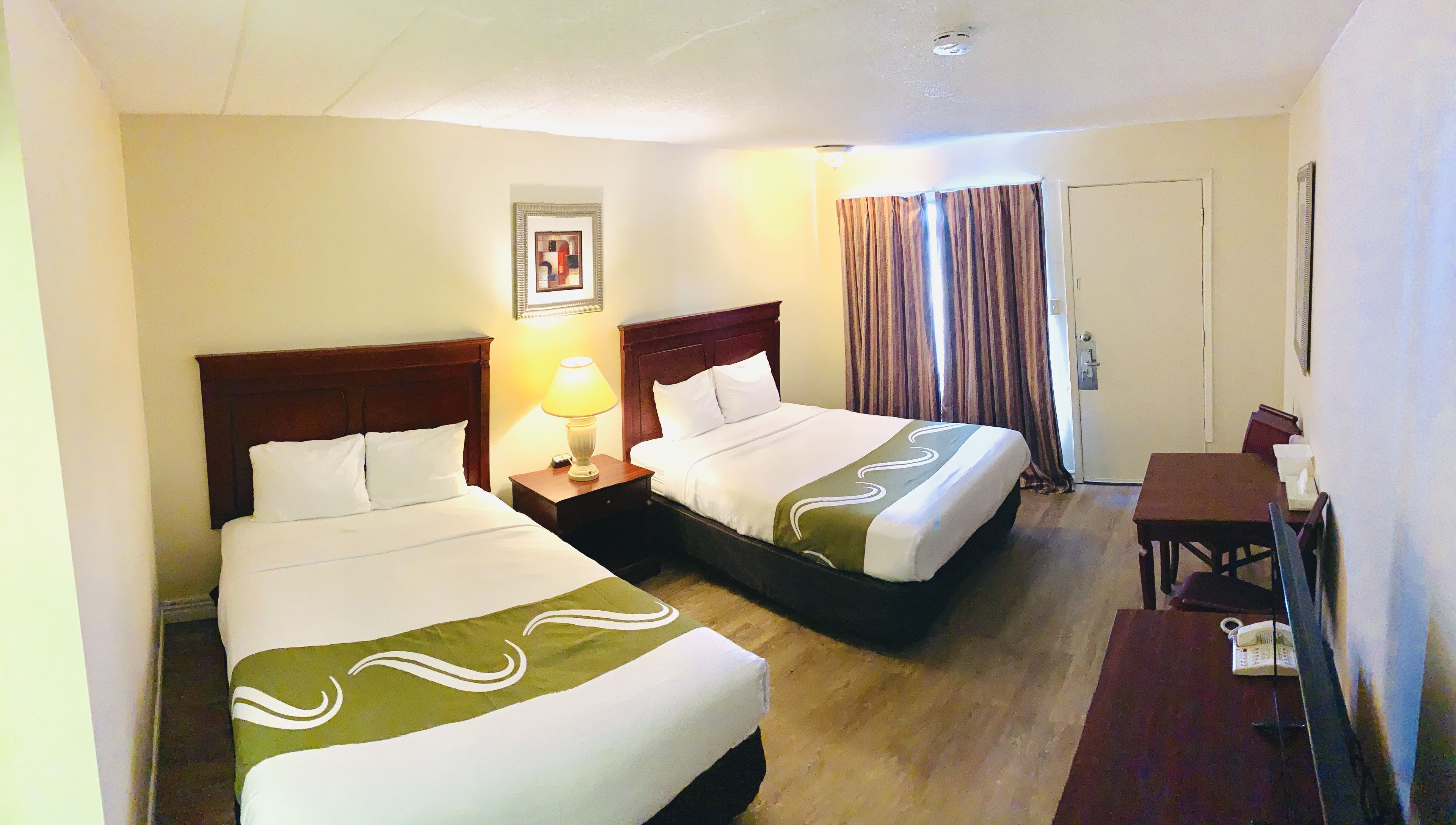 A hotel room with two single beds, a desk with a chair, a telephone, and a door.