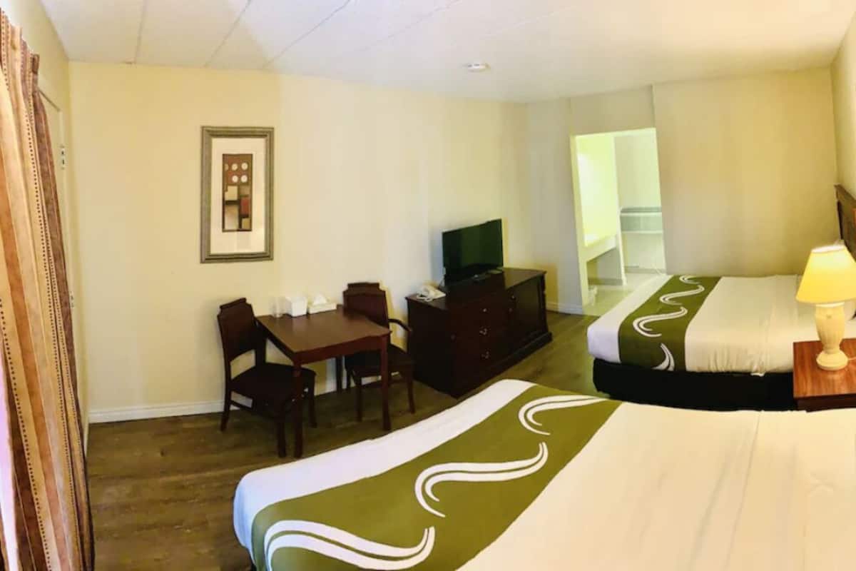 Une chambre d’hôtel avec deux lits, un bureau avec une télévision, une chaise et une commode.