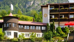 Un chalet traditionnel doté d’une tour, d’un balcon fleuri et surplombant un paysage montagneux.