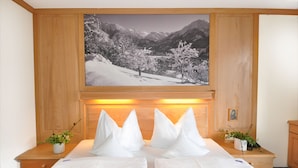 Une chambre d’hôtel avec un lit, deux tables de chevet ornées de plantes en pot, un grand tableau encadré représentant un paysage enneigé et un lambris en bois.