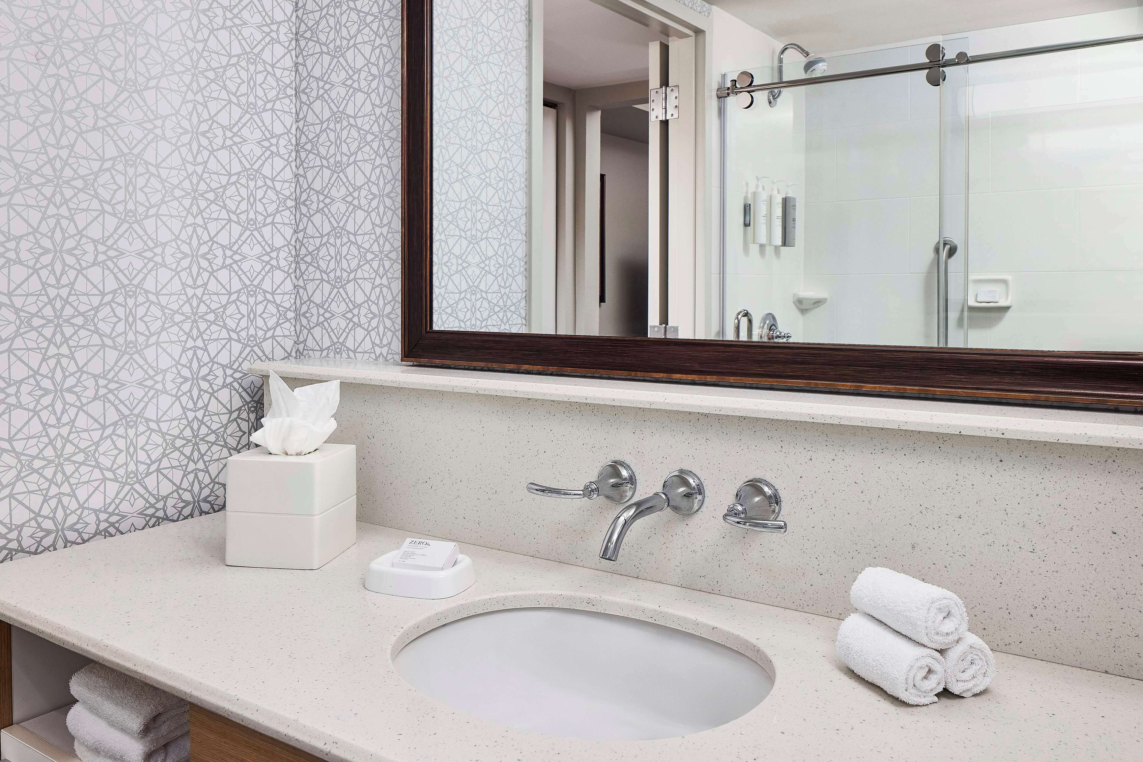A bathroom with a large mirror, a sink, and a towel rack.