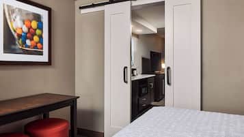 Ein Hotelzimmer mit Bett, Schreibtisch, einem roten Hocker, einem Kleiderschrank und einem gerahmten Bild an der Wand.