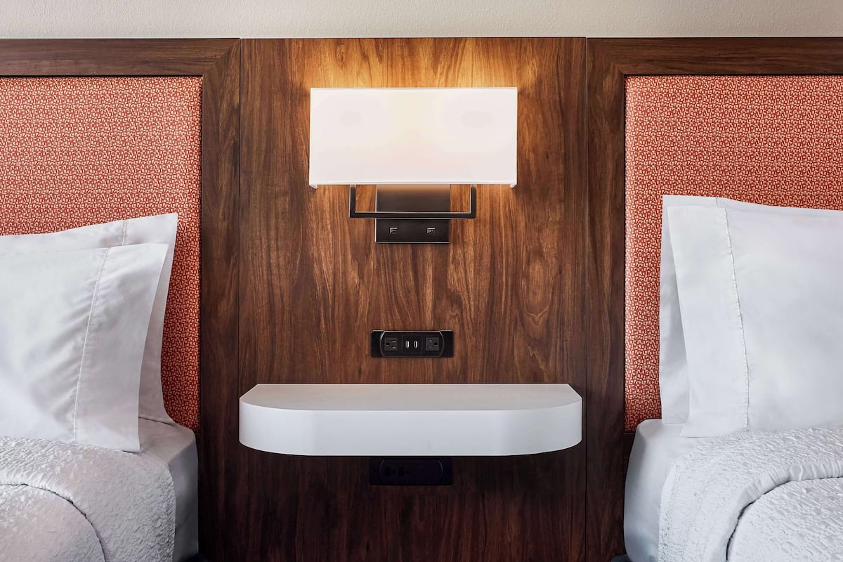 A hotel room with a wooden headboard, a bedside table, and a wall-mounted light fixture.