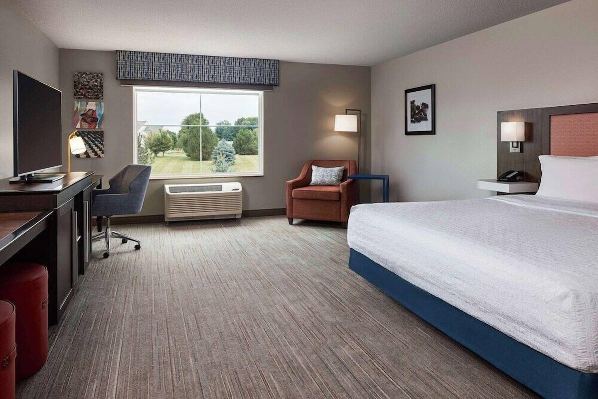 A hotel room with a bed, desk, chair, TV, and a window with a view.