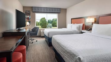 Habitación de hotel con dos camas, un escritorio, una silla, un televisor y una ventana con vistas a árboles.
