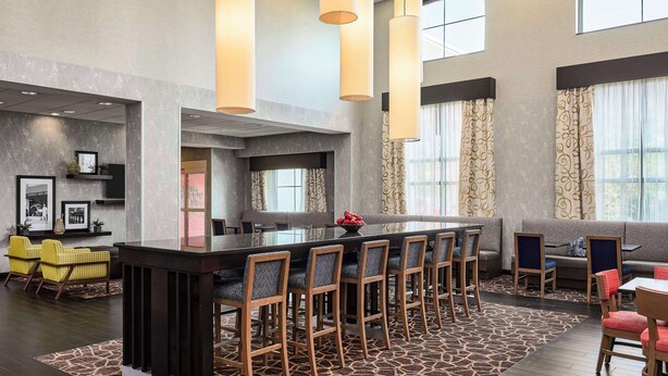 A modern hotel lobby with a central bar, seating areas, and large windows.