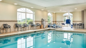 A swimming pool with chairs and tables, large windows, and a view of greenery.