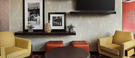 A modern living room with patterned yellow chairs, a black ottoman, and framed pictures on shelves.