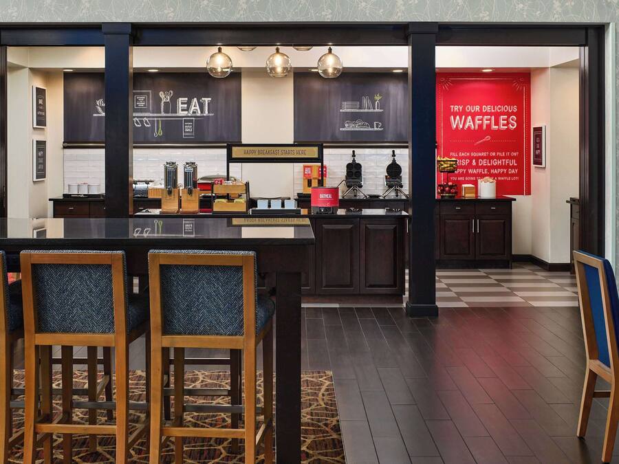 A modern cafe with a checkered floor, wooden chairs, and a red waffle sign.