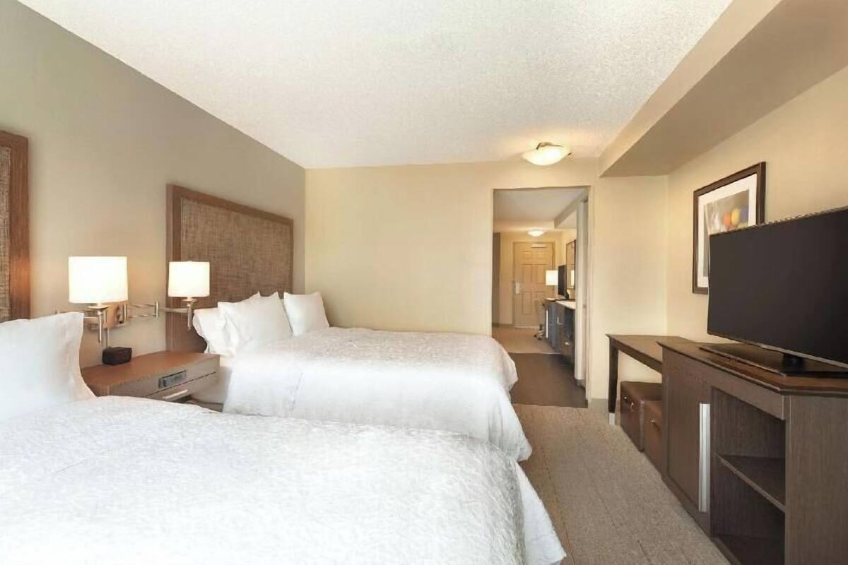 A hotel room with two beds, a TV, a desk, and a bathroom visible through an open door.