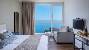 Habitación de hotel con cama, sofá, televisión y vistas al mar.