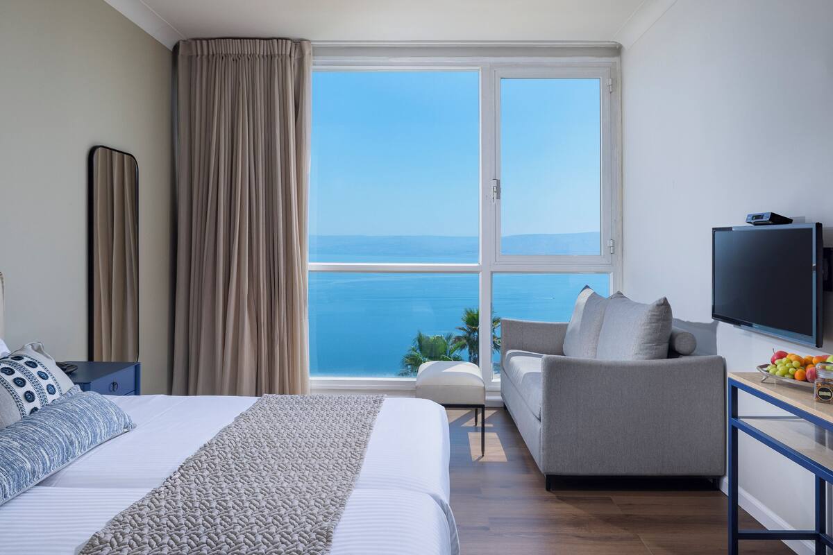 Habitación de hotel con cama, sofá, televisión y vistas al mar.