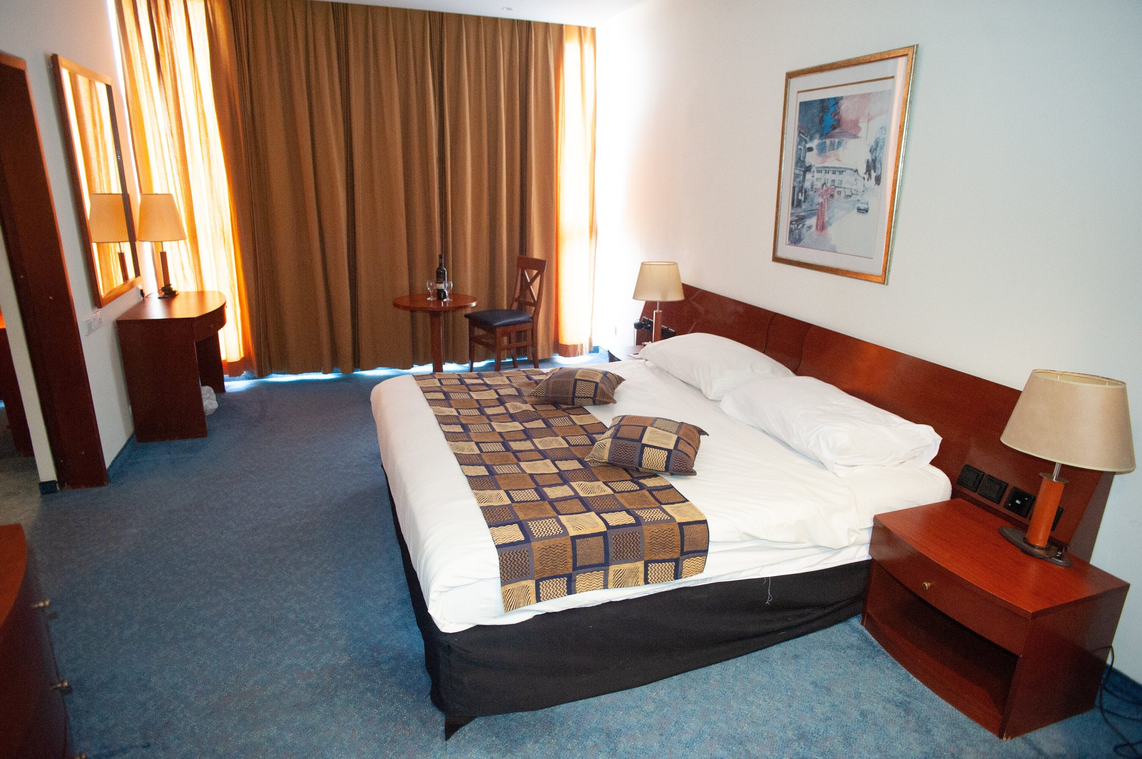 Una camera d'albergo con un letto grande, una scrivania, una sedia, un tavolino e un quadro appeso al muro.