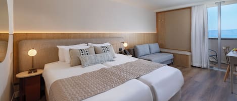 Habitación de hotel con una cama grande, un sofá, un escritorio y vista al mar.