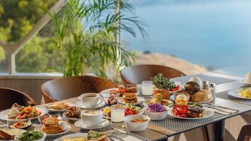 Una tavola imbandita con diversi prodotti per la colazione, tra cui pasticcini, frutta e bevande, con una vista panoramica sullo sfondo.