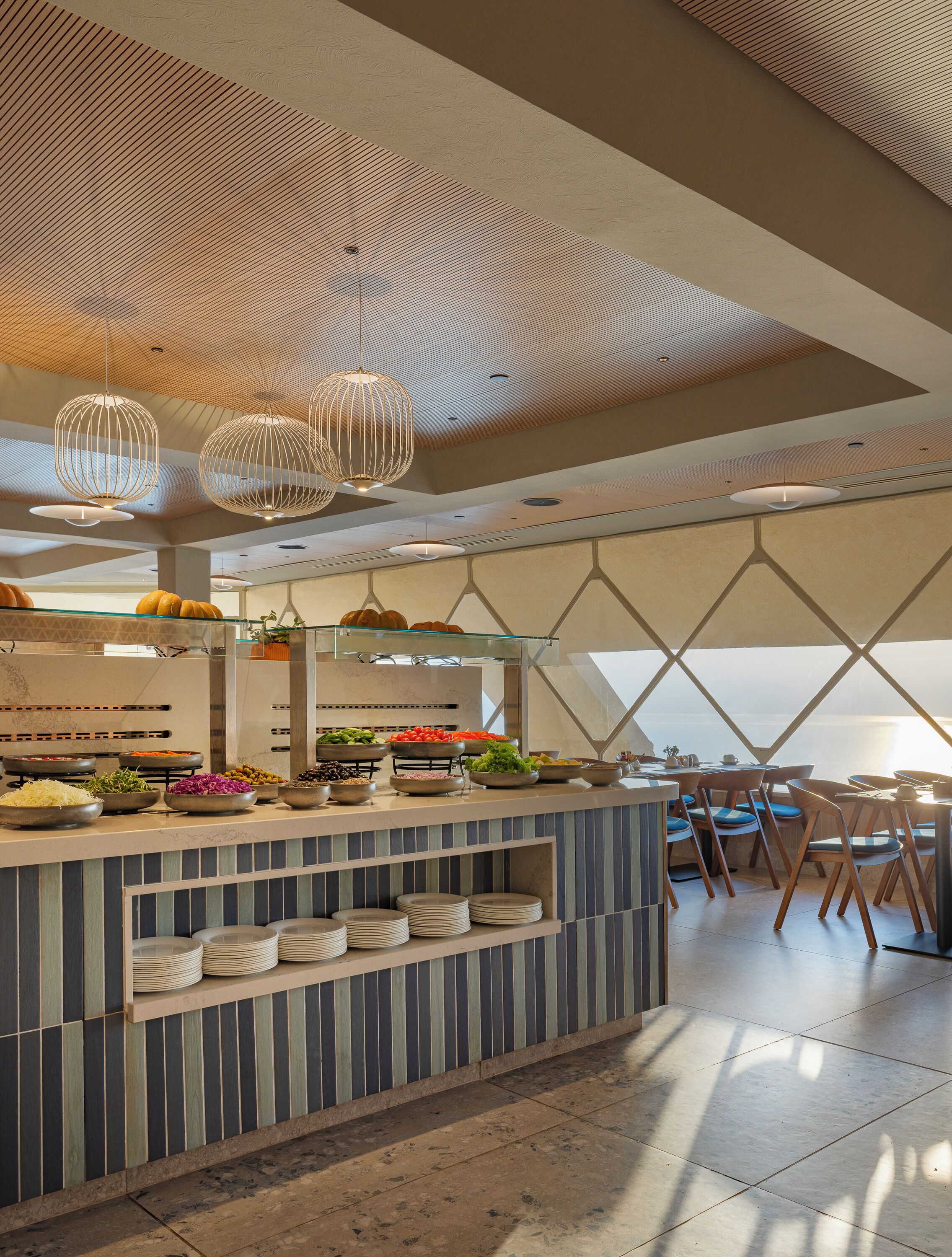 A modern restaurant with a buffet, hanging light fixtures, and a view of the sea.
