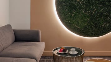 Una sala moderna con un sofá gris, una decoración de musgo verde montada en la pared y una pequeña mesa redonda con una silla verde.