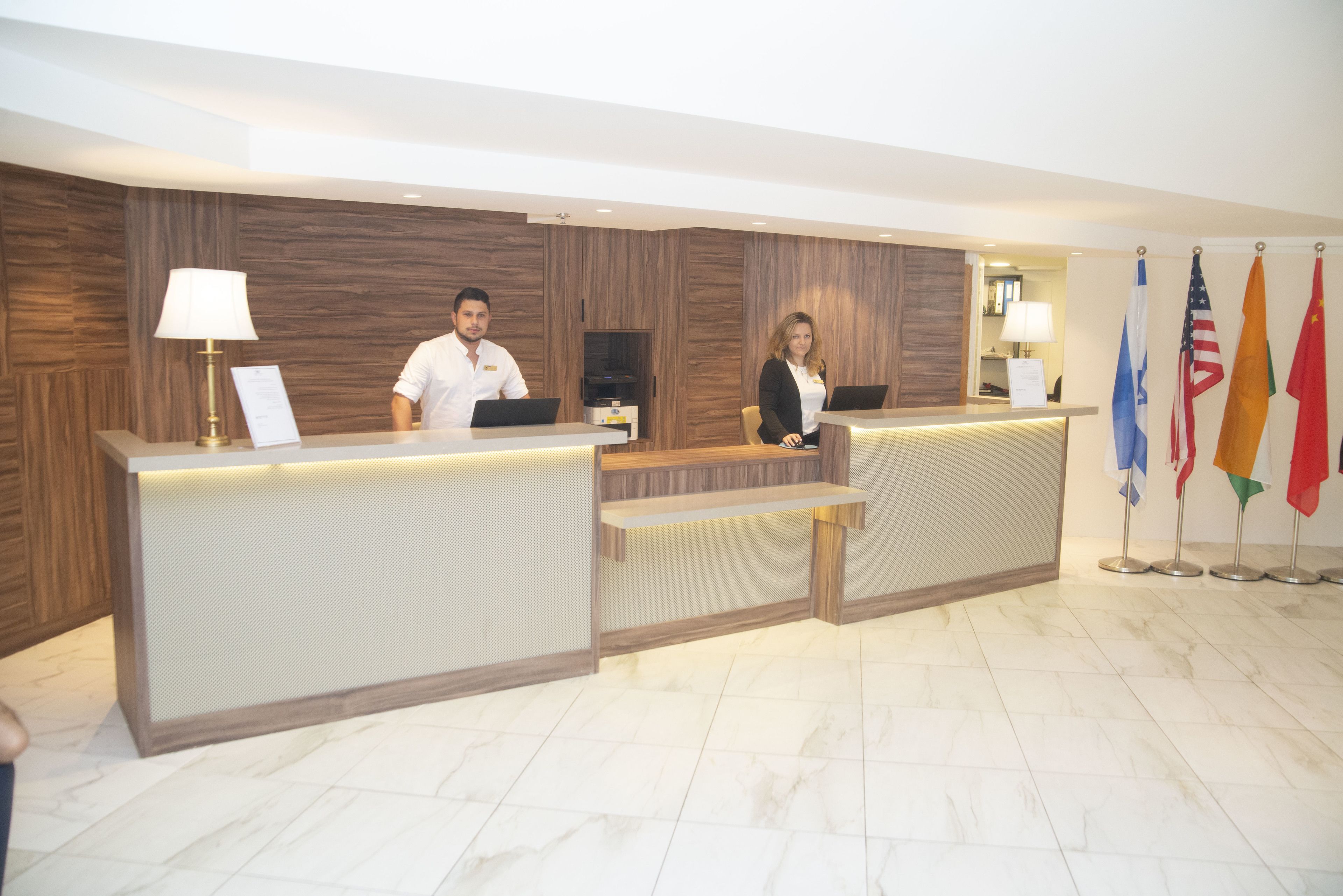 Un mostrador de recepción con dos empleados, una pared de madera y banderas.