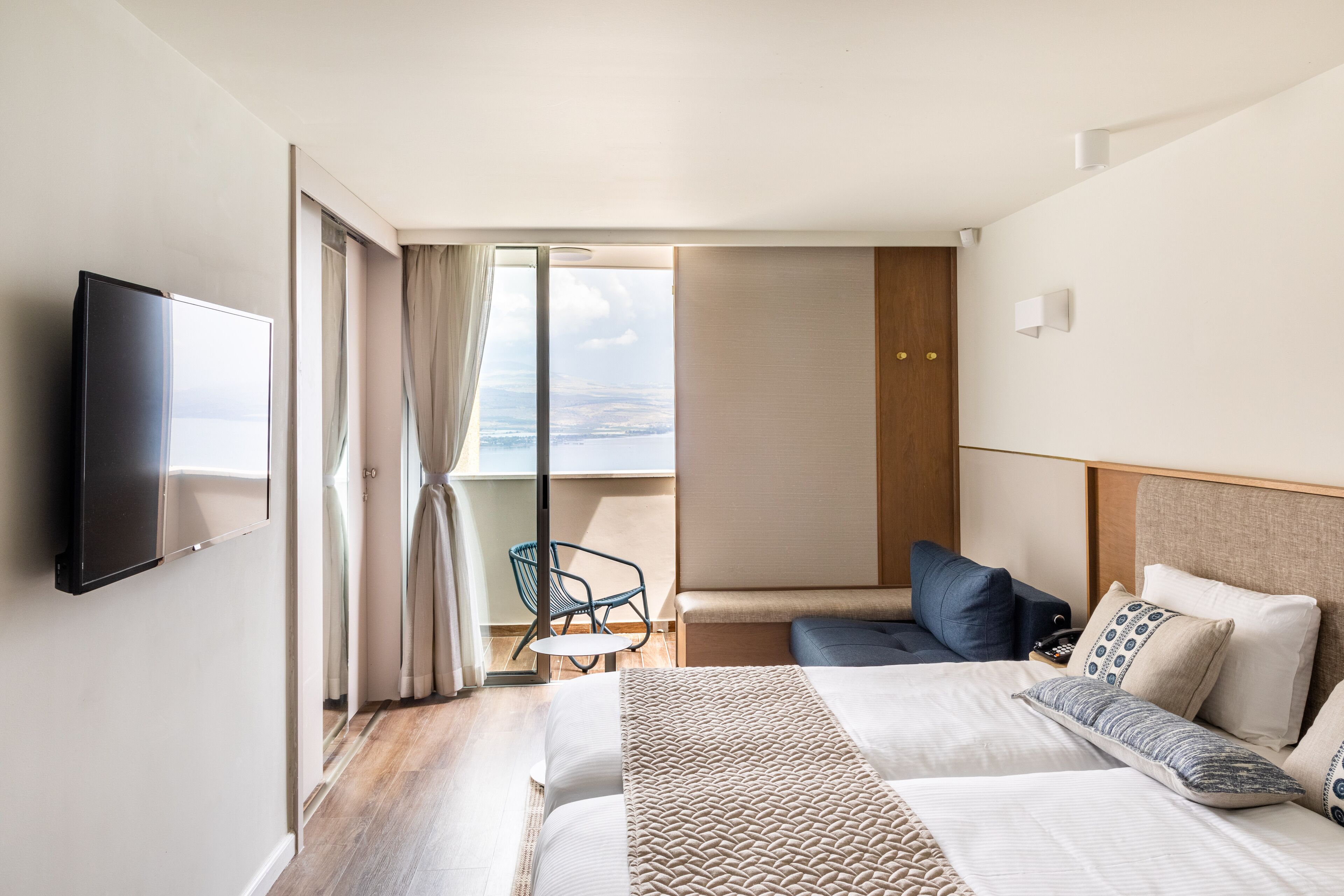 A hotel room with a bed, a TV, a chair, and a view of the sea.