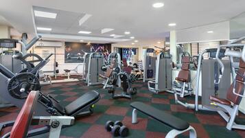 A gym with various exercise machines, a bench, and dumbbells.